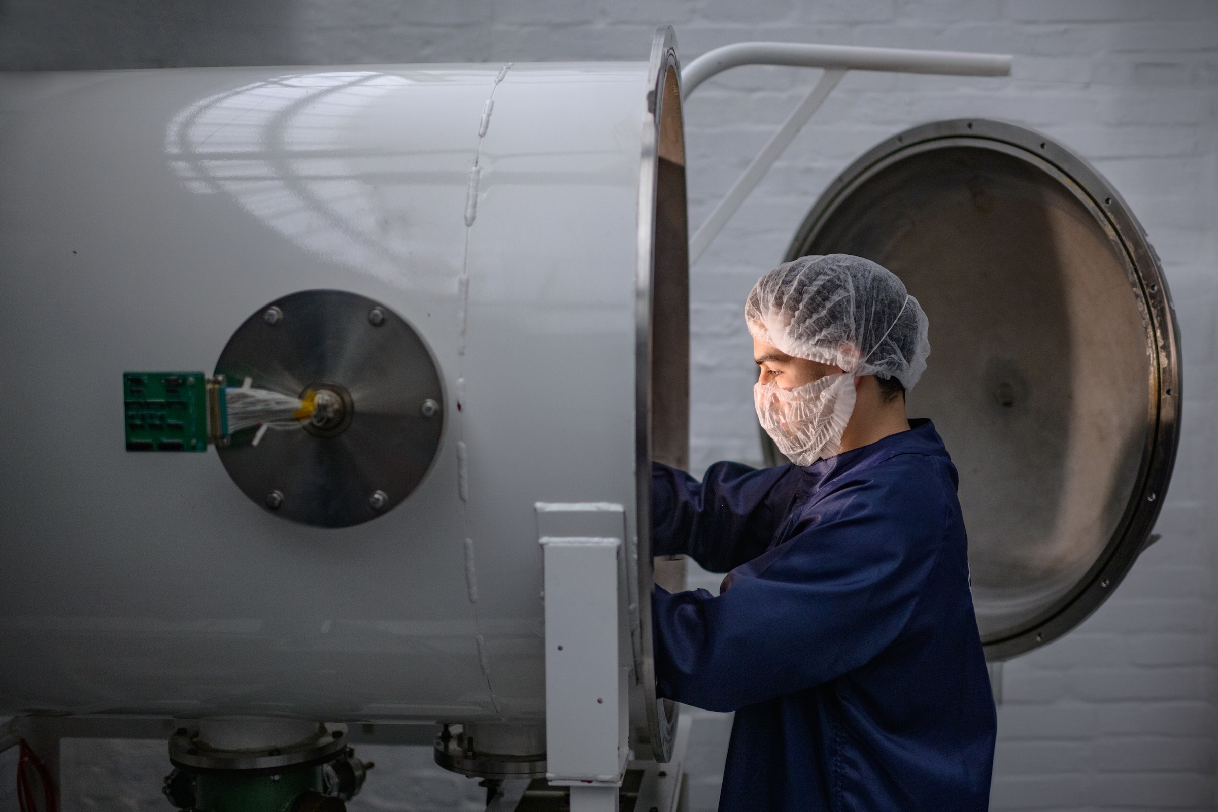 Engineer with mask handling a component inside a testing chamber