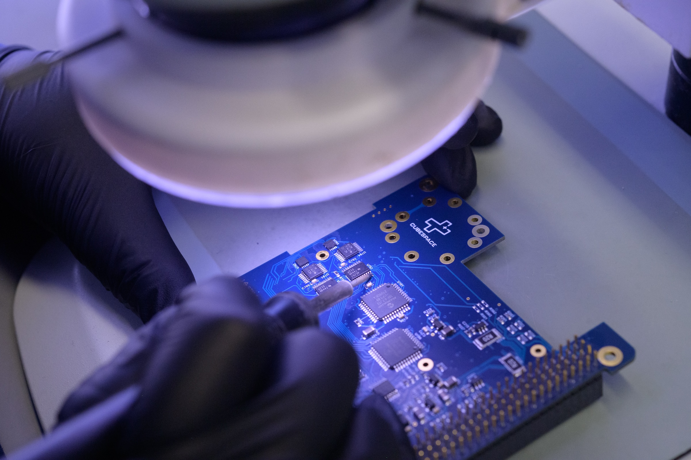 A CubeSpace engineer looking at a circuit through a microscope